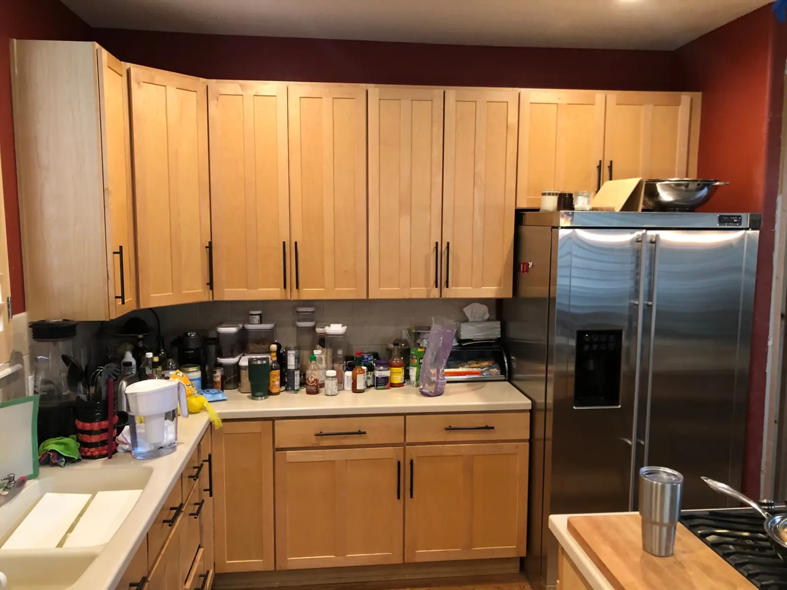 Kitchen with deep red walls and natural maple cabinets before painting
