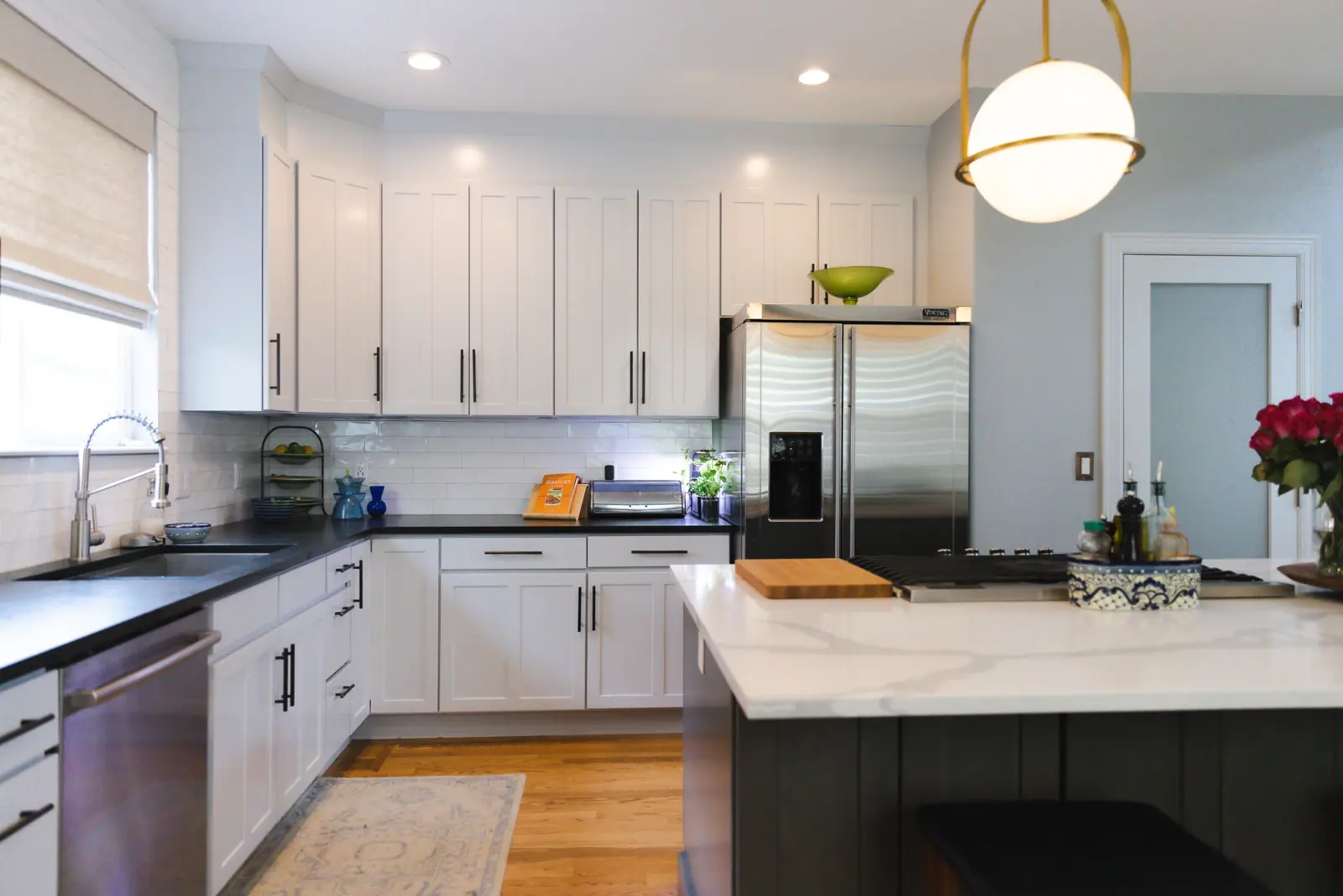 The same kitchen after painting, with white shaker cabinets, black hardware and soft blue-gray walls