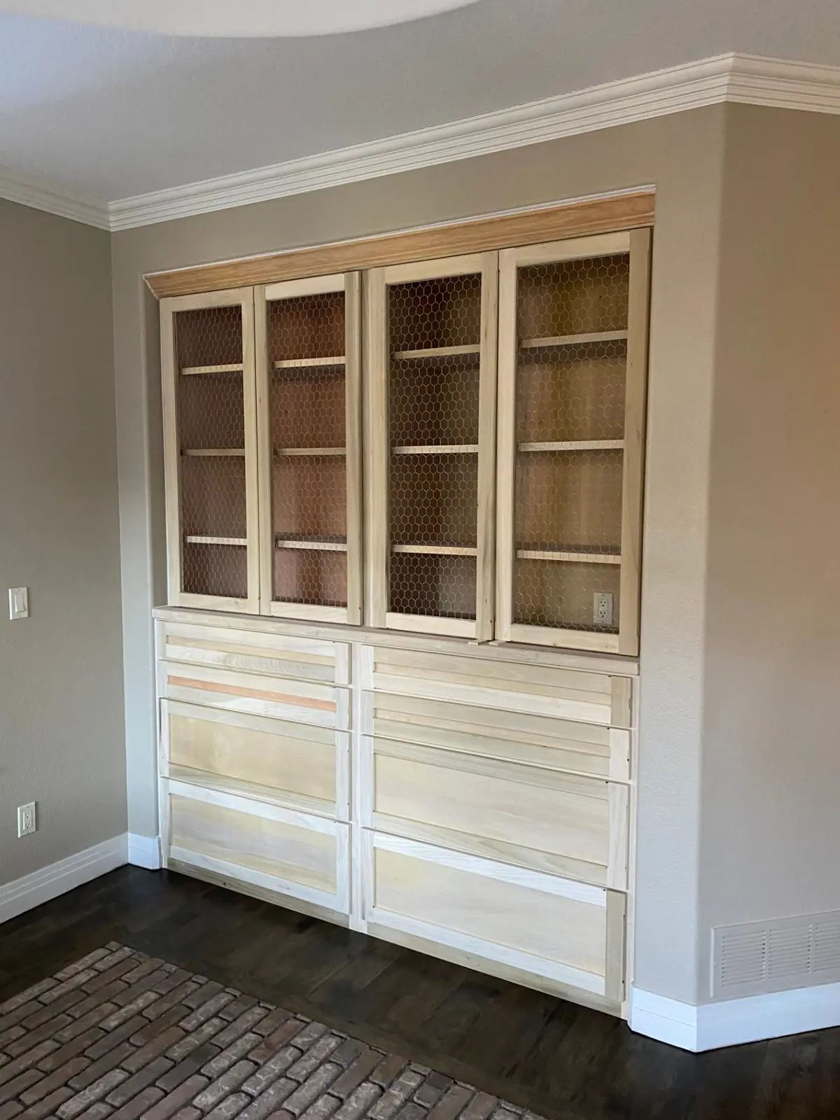 Unfinished raw wood built-in hutch with chicken-wire doors against tan dining room walls